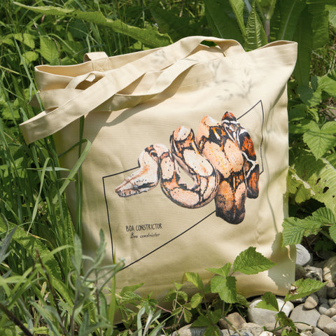 Product photo of our boa constrictor tote bag, here standing in nature between plants.