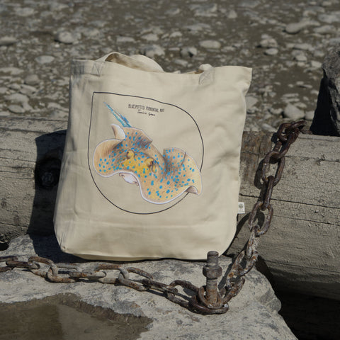 Bluespotted ribbontail ray tote bag, photographed on the beach. Made from 100% organic cotton.