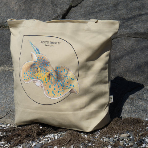 Bluespotted ribbontail ray tote bag, photographed on the beach. Made from 100% organic cotton.