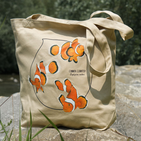 Outdoor product photo of our common clownfish organic tote bag hanging standing outside on rocks.