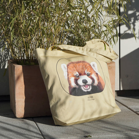 Our organic cotton tote bag with a cheeky red panda print outside in sunlight.