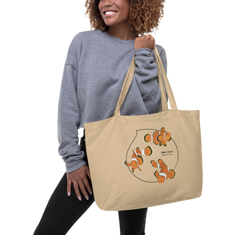 Product mockup of our large organic tote bag and a print of 3 hand-drawn common clownfishes. Here the bag is held by a model.