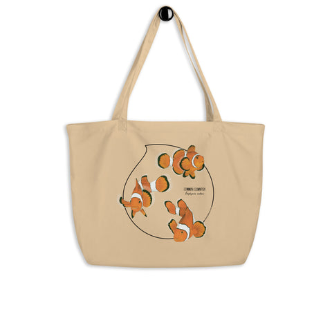 Product mockup of our large organic tote bag and a print of 3 hand-drawn common clownfishes. Here the bag hangs from its handles.