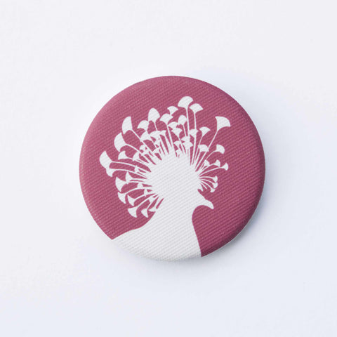 A red, fabric-covered magnet with the silhouette of a Victoria crowned pigeon is lying on a white surface.