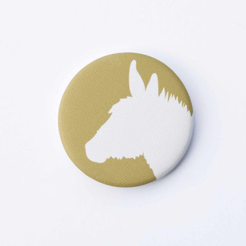 A gold-yellow, fabric-covered magnet with the silhouette of a donkey on a flat white surface.