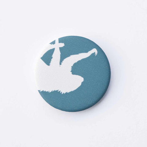 A teal-blue, fabric-covered magnet with the silhouette of a two-fingered sloth on a flat white surface.
