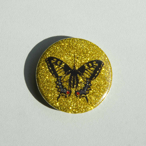 A beautiful sparkly magnet shows a swallowtail butterfly on a golden-glittery background.