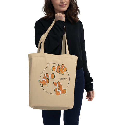 Product mockup of our organic tote bag featuring a print of 3 hand-drawn common clownfishes. Here the bag hangs from the hands of a model.