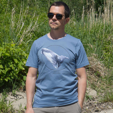 Male model outdoor on a beach wearing a steel blue t-shirt with a humpbak whale print.