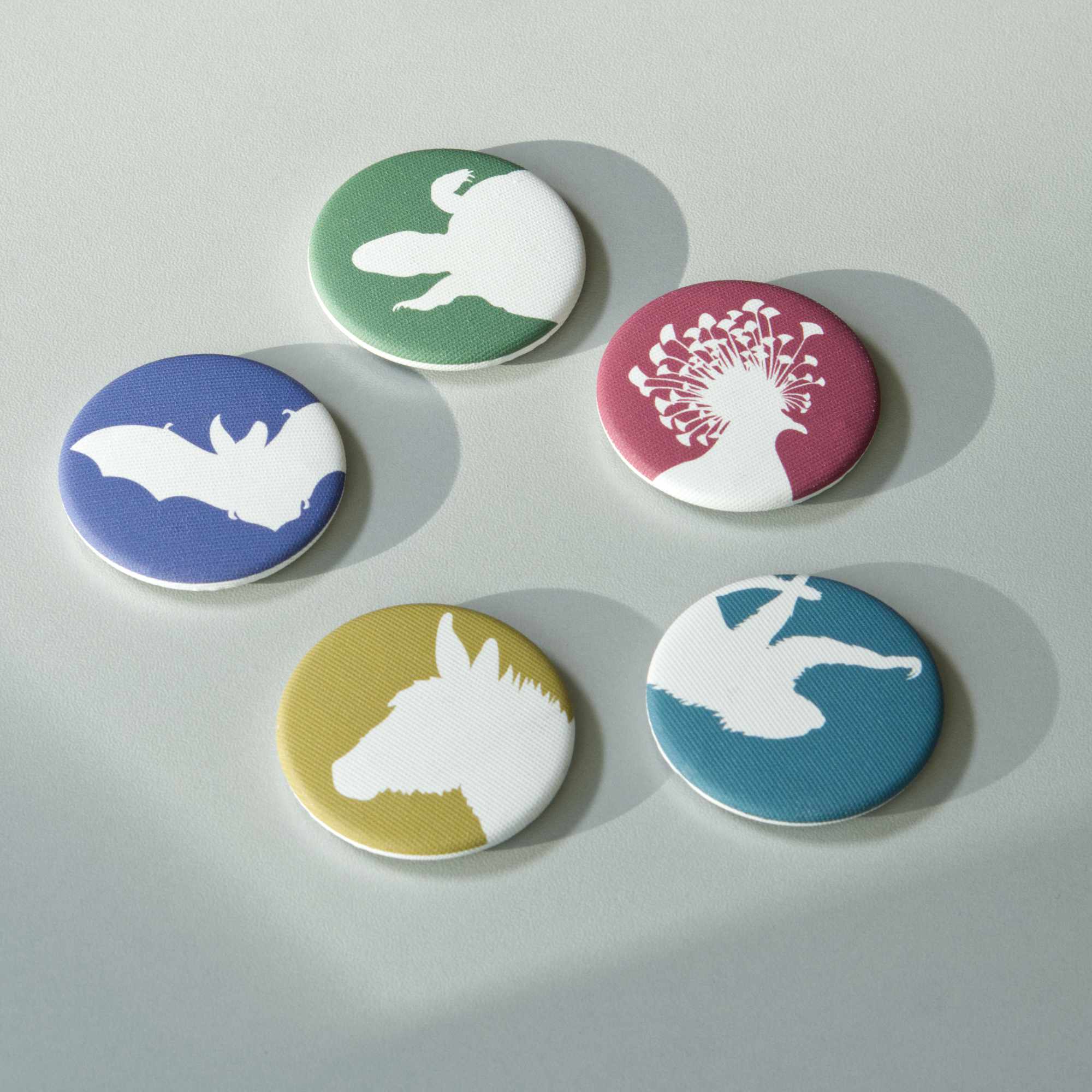Five different coloured, fabric-covered magnets on a white surface. All feature the white silhouette of a different animal.