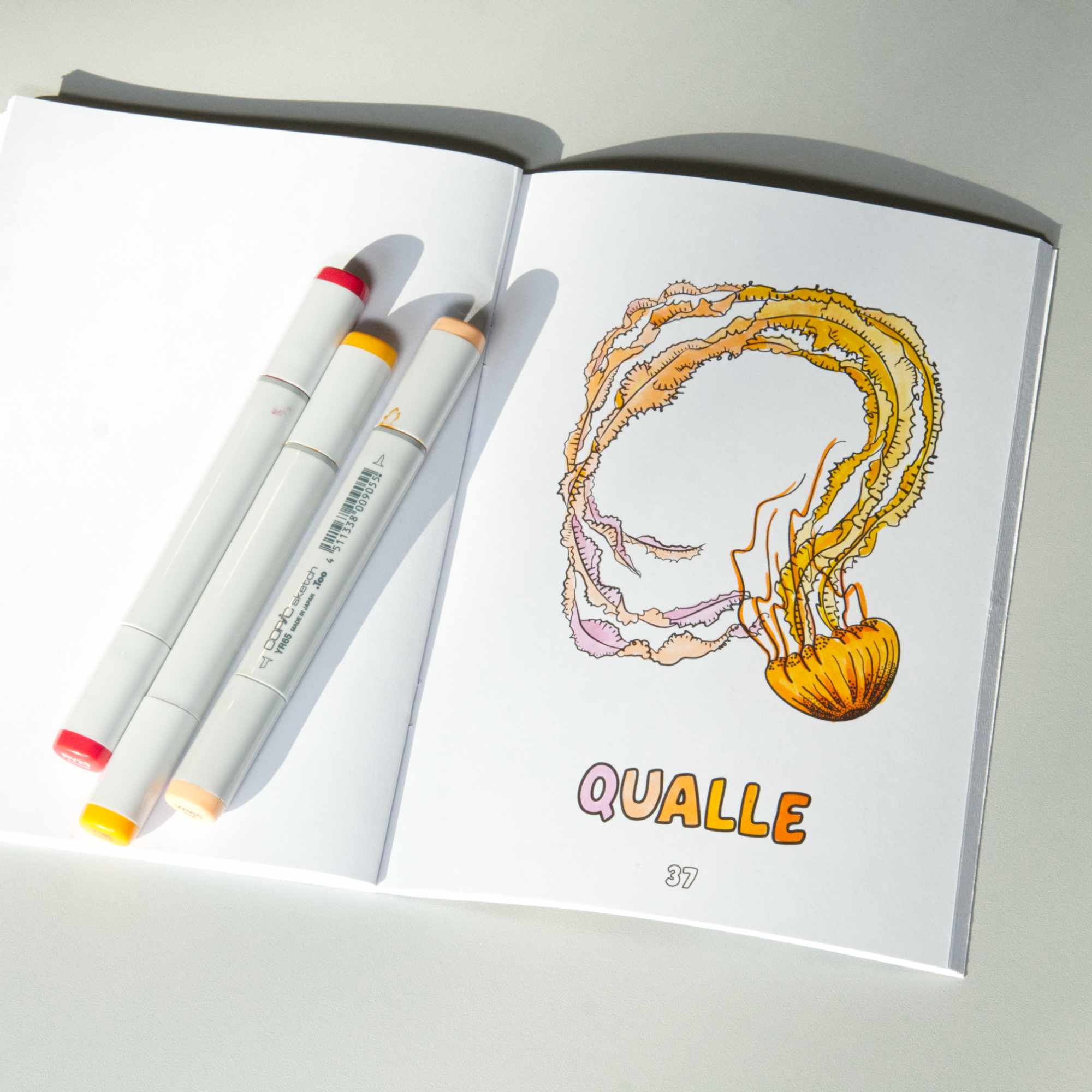 Colouring book open on the page with the letter Q and an qualle (jellyfish in German), coloured-in as an example.