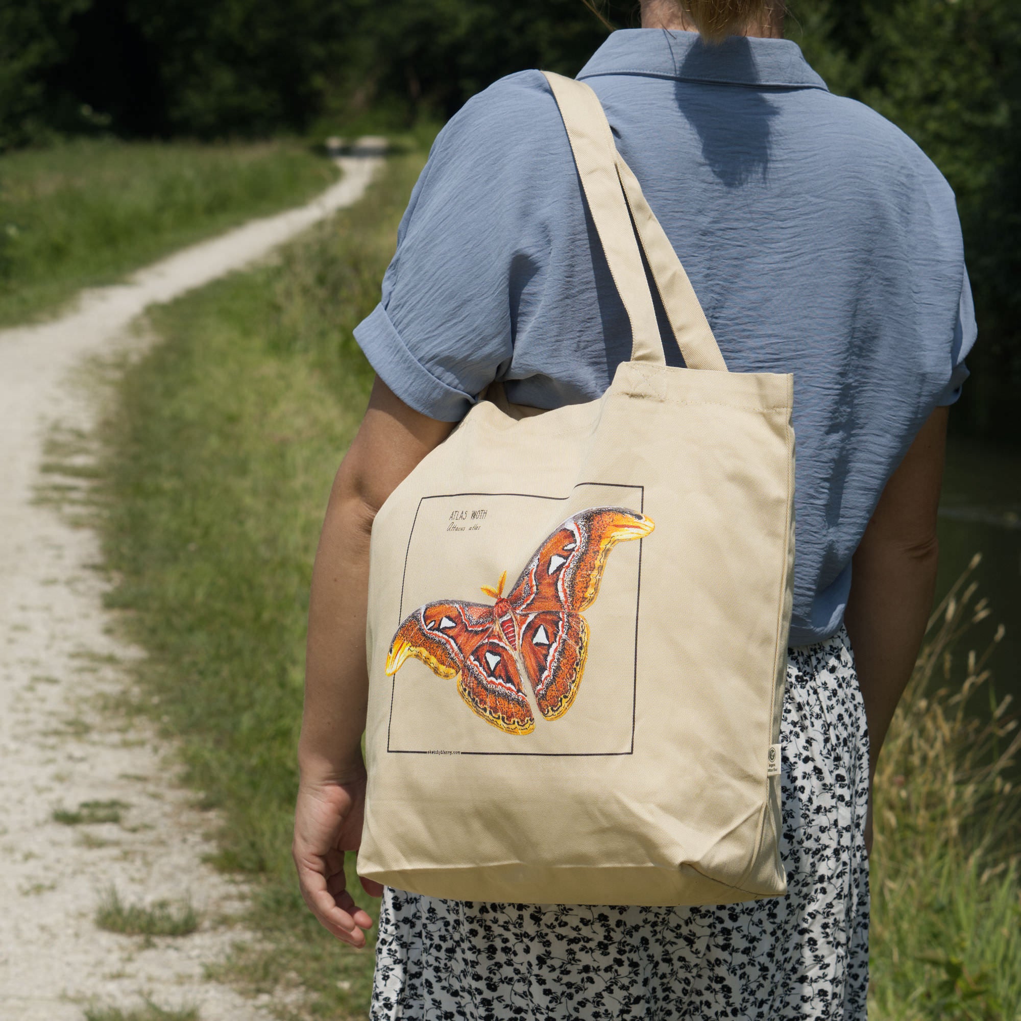 Product photo of our atlas moth organic tote bag. Here seen over the shoulder of a model outside.