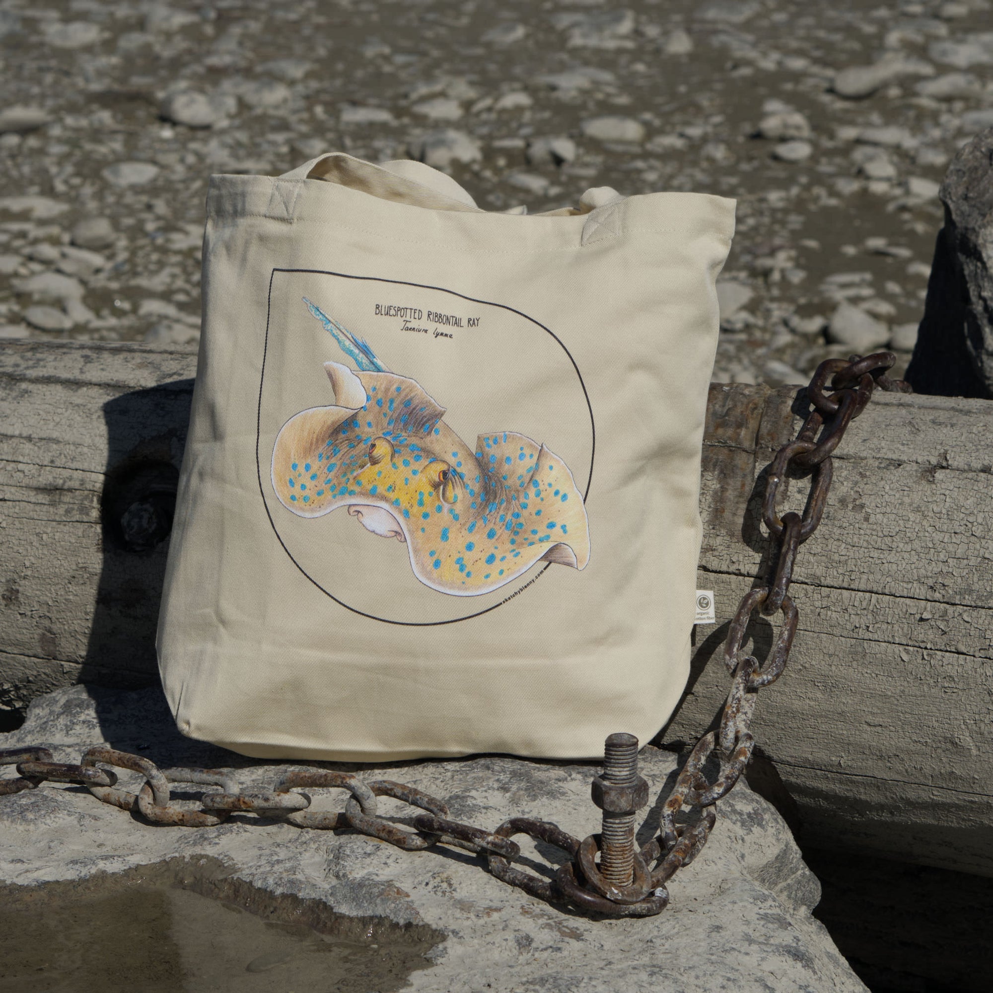 Bluespotted ribbontail ray tote bag, photographed on the beach. Made from 100% organic cotton.