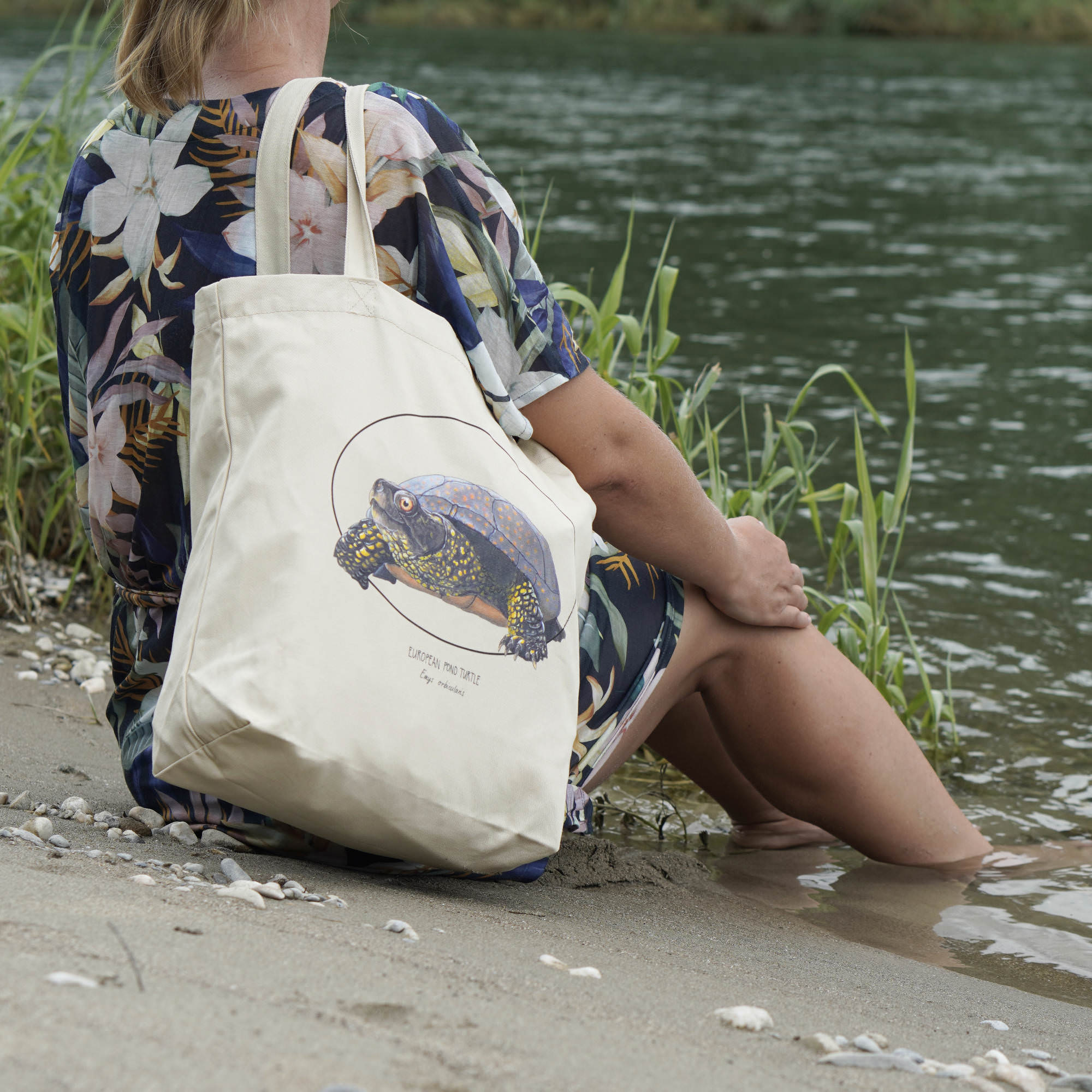 Photo of our tote bag on a model on a beach. This sturdy bag features a print of a hand-drawn European pond turtle. 100% organic cotton. Beach bag, shopping bag, travel bag, or just as a present.