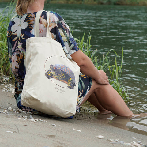 Photo of our tote bag on a model on a beach. This sturdy bag features a print of a hand-drawn European pond turtle. 100% organic cotton. Beach bag, shopping bag, travel bag, or just as a present.