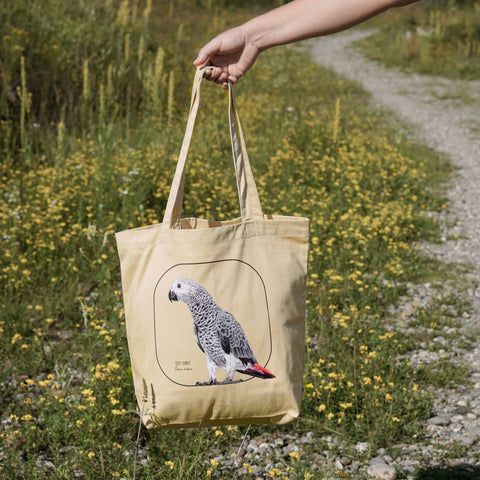 Our tote bag with a model outside. This sturdy bag comes with a beautiful print of a hand-drawn juvenile grey parrot. 100% organic cotton. Beach bag, shopping bag, travel bag, or just as a present. PETA-approved vegan.