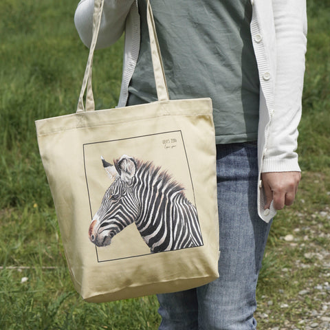 A model in sunlight carrying our tote bag with a beautiful print of a hand-drawn Grévy's Zebra. 100% organic cotton. Beach bag, shopping bag, travel bag, or just as a present.