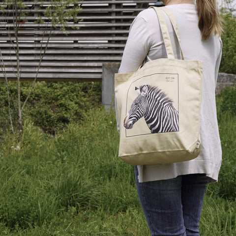 A model in sunlight carrying our tote bag with a beautiful print of a hand-drawn Grévy's Zebra. 100% organic cotton. Beach bag, shopping bag, travel bag, or just as a present.