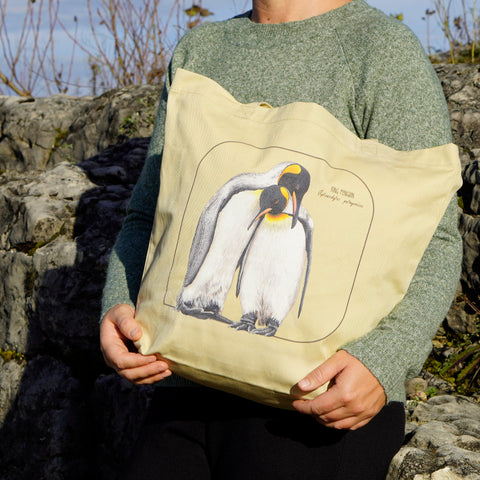 A model holding of our tote bag in sunlight. It comes with a beautiful print of a hand-drawn pair of king penguins huddled together. 100% organic cotton. Beach bag, shopping bag, travel bag, or just as a present.