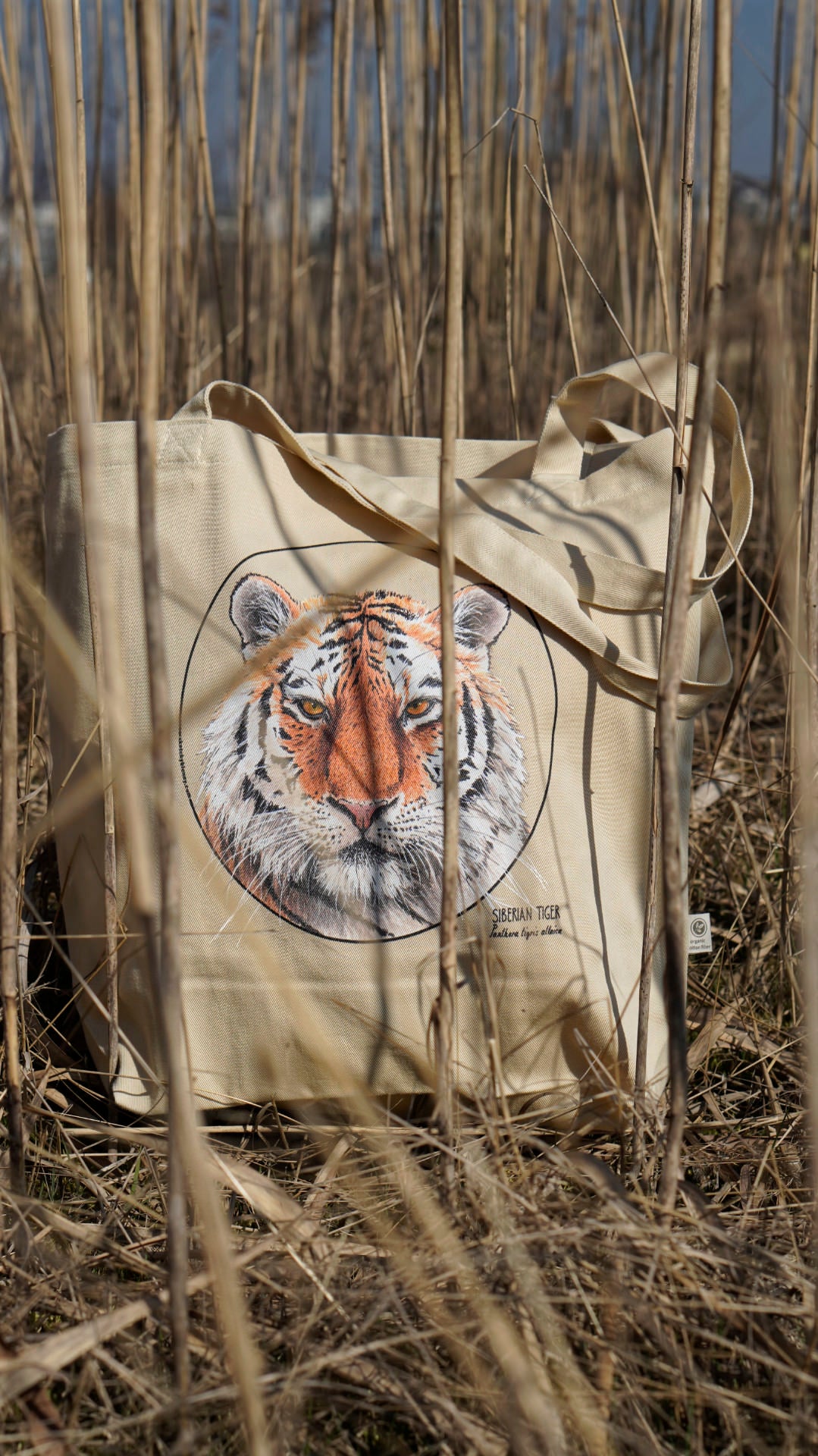 Our organic tote bag with a Siberian tiger print outside amongst tall grass