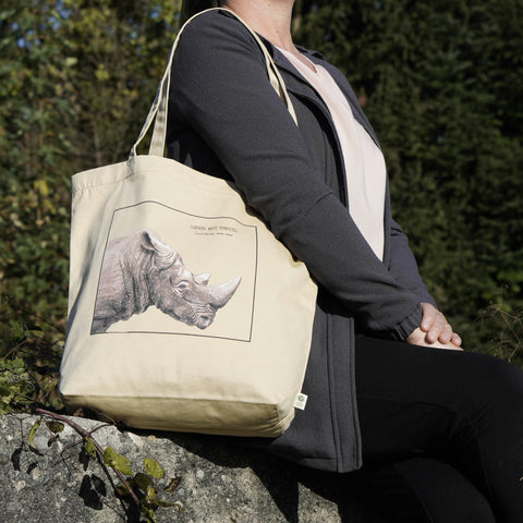 Our tote bag on a model in sunlight. A beautiful, carefully drawn southern white rhinoceros is printed on the front side of the bag.