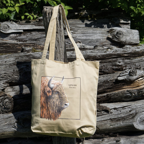 Product photo of our european bison (wisent) tote bag outside in sunlight, hanging from a wooden pole.