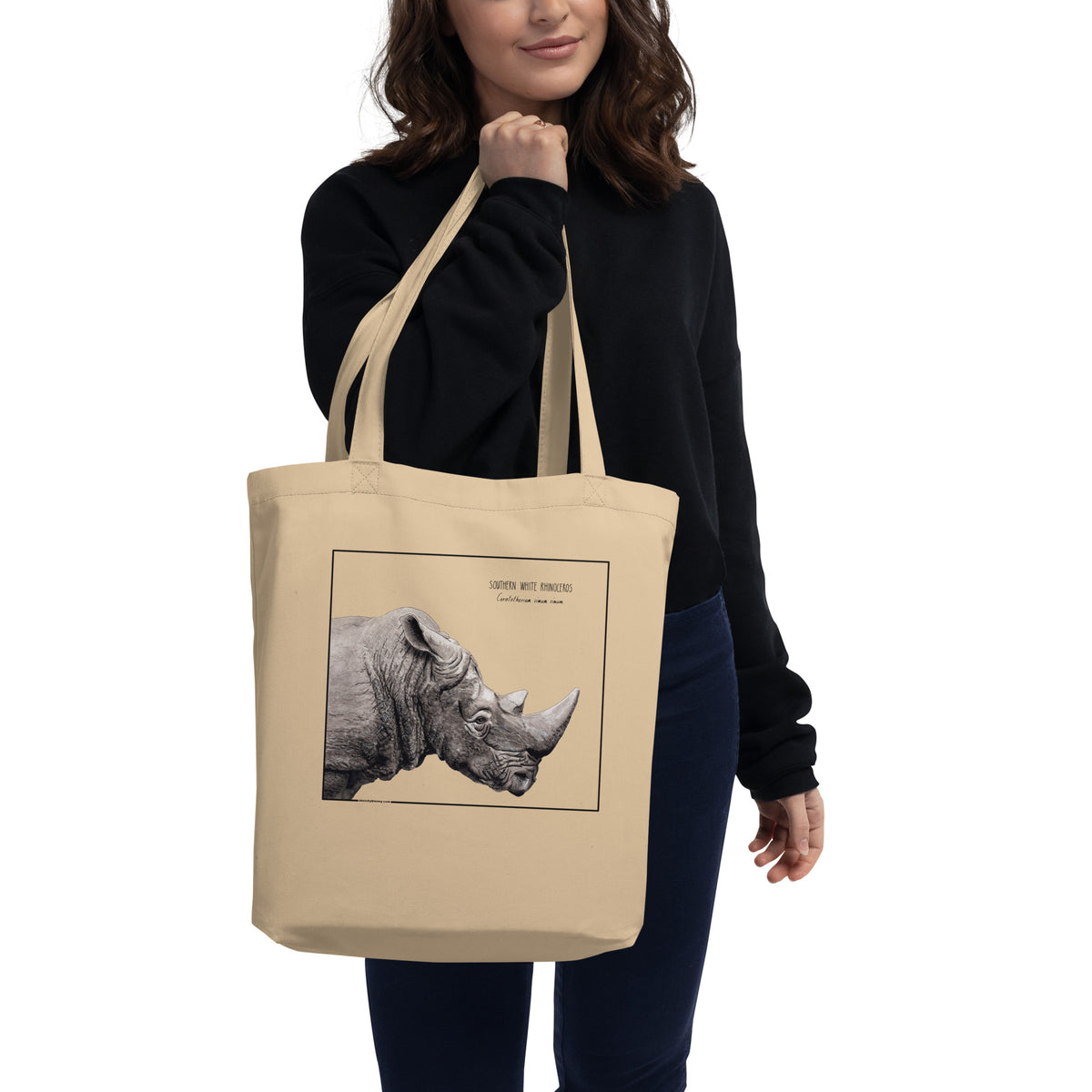 Product mockup of our tote bag with beautiful, carefully drawn southern white rhinoceros printed on the front side of the bag. Here shown being held by a model