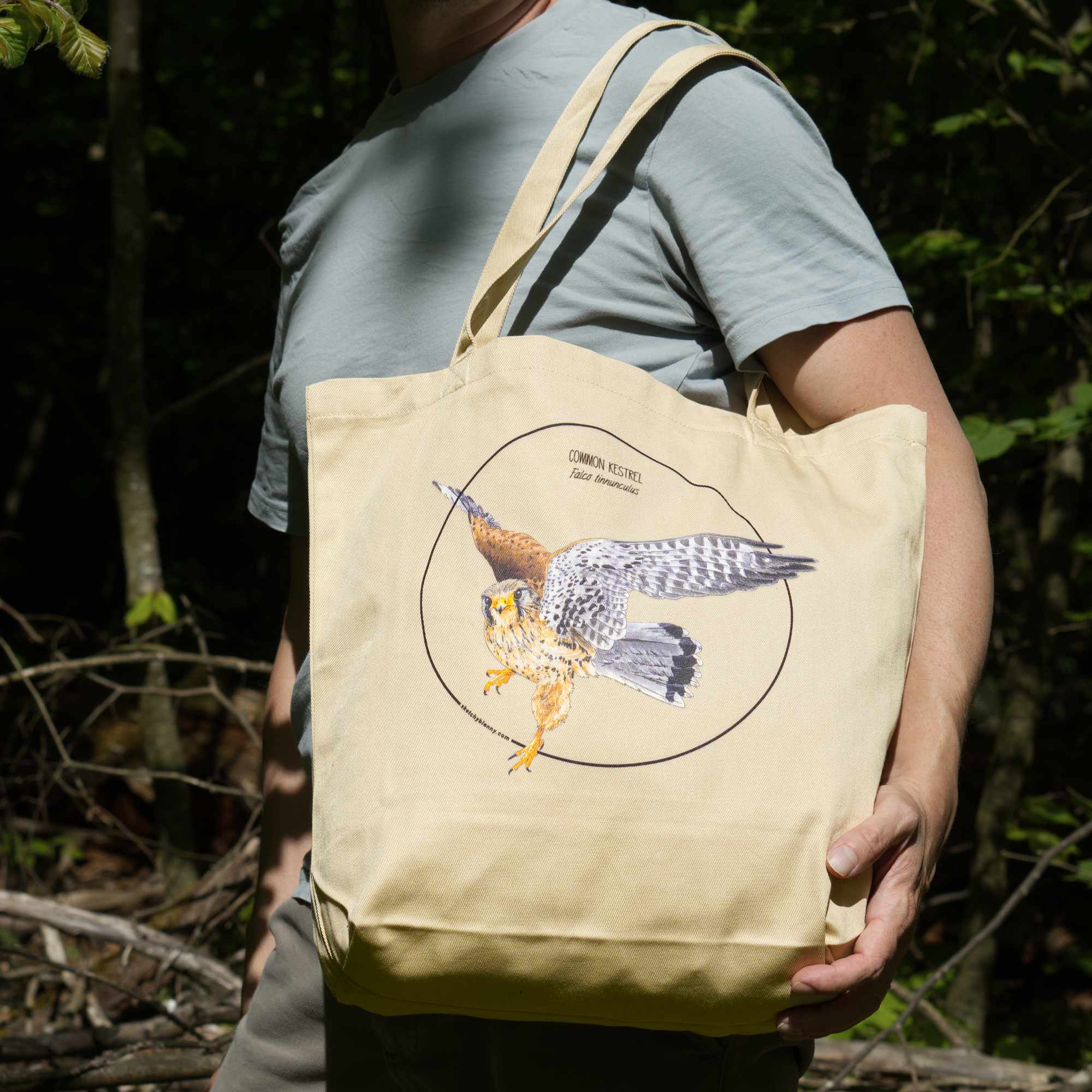 Outdoor photo of the organic cotton tote bag with a kestrel print, being held by a model.