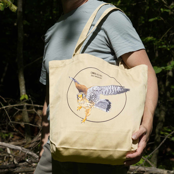 Outdoor photo of the organic cotton tote bag with a kestrel print, being held by a model.