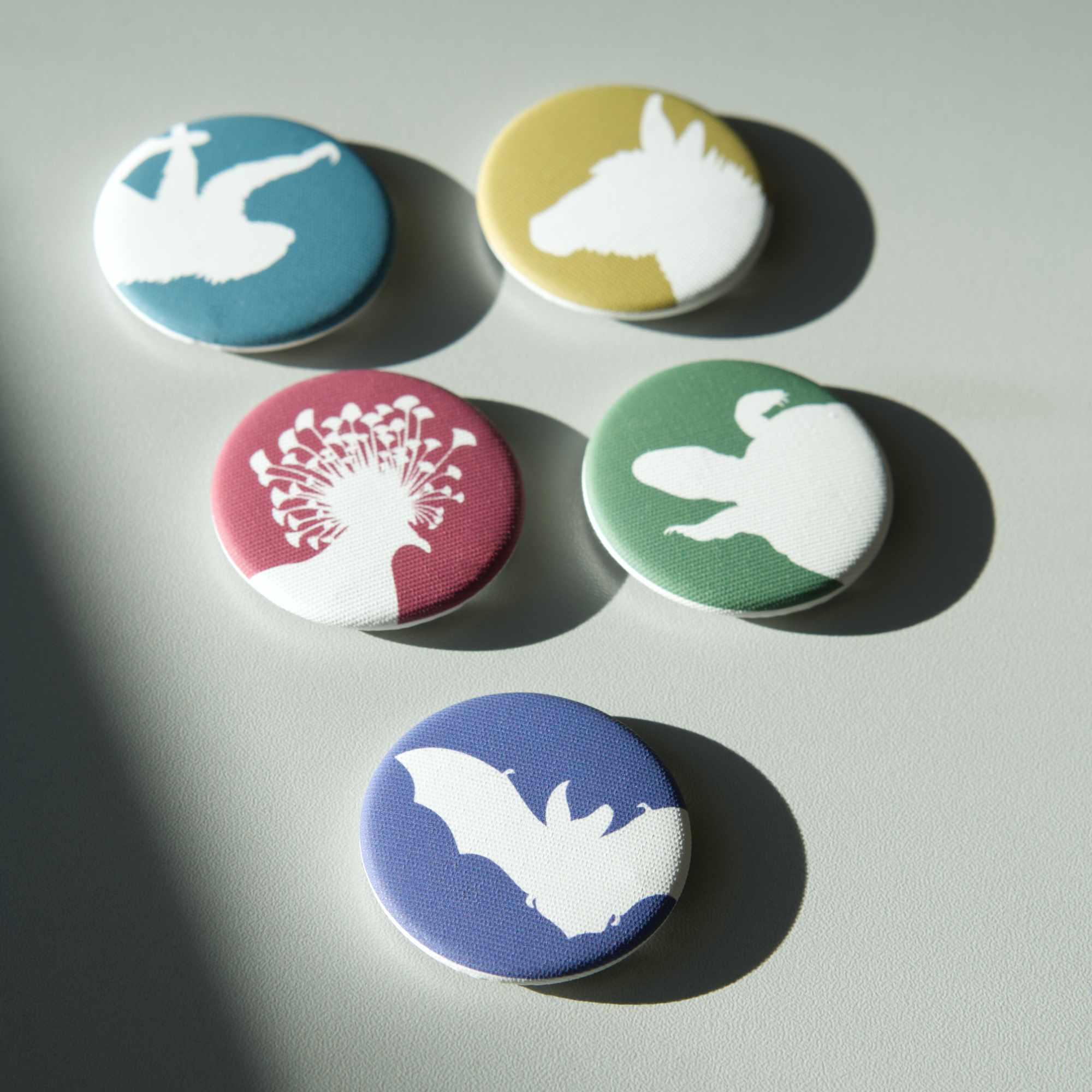 Five different coloured, fabric-covered magnets on a white surface. All feature the white silhouette of a different animal.