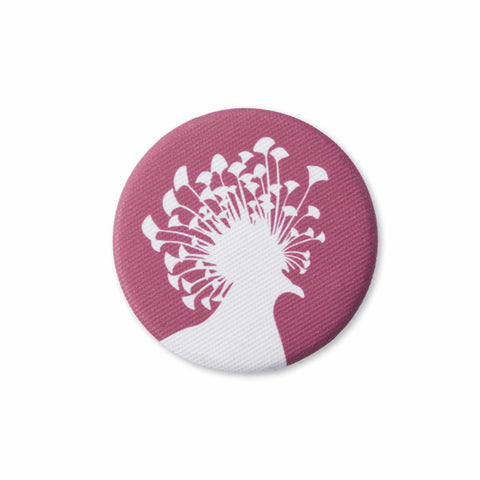A red, fabric-covered magnet with the silhouette of a Victoria crowned pigeon is lying on a white surface.