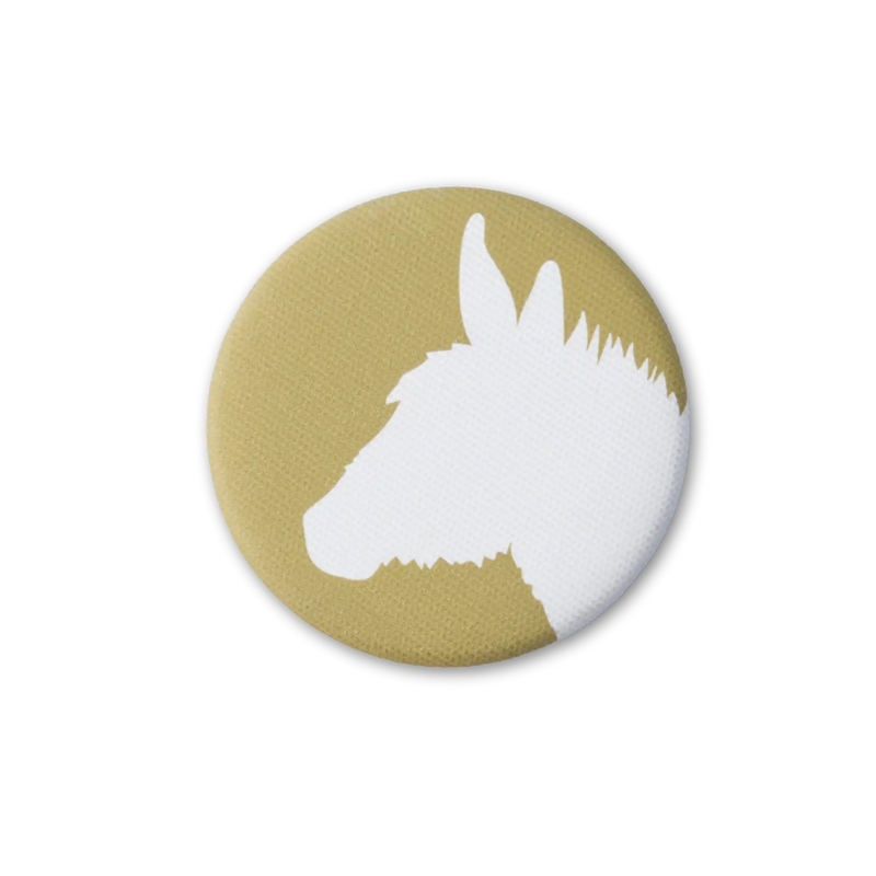 A gold-yellow, fabric-covered magnet with the silhouette of a donkey on a flat white surface. Top down photo.