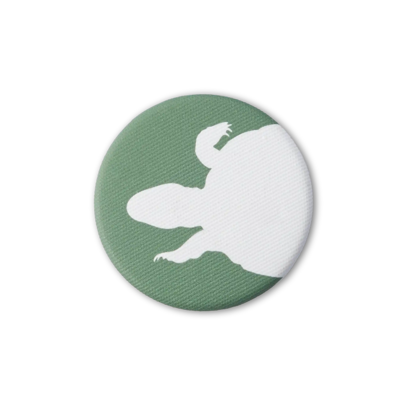 Green fabric-covered magnet with the white silhouette of a swimming turtle from above. Photo from top down.