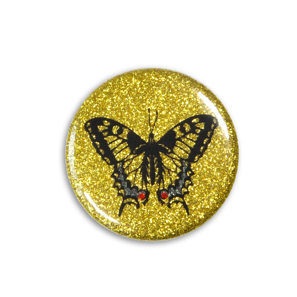A beautiful sparkly magnet shows a swallowtail butterfly on a golden-glittery background. Photo from top down.