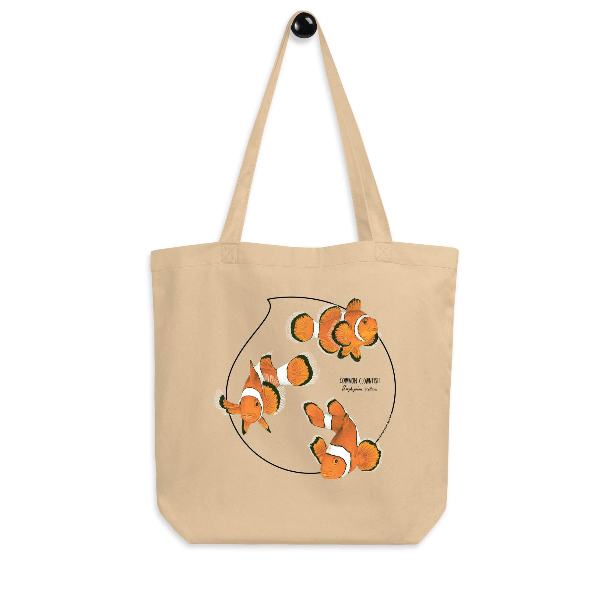 Product mockup of our organic tote bag featuring a print of 3 hand-drawn common clownfishes. Here the bag hangs from it's handles.