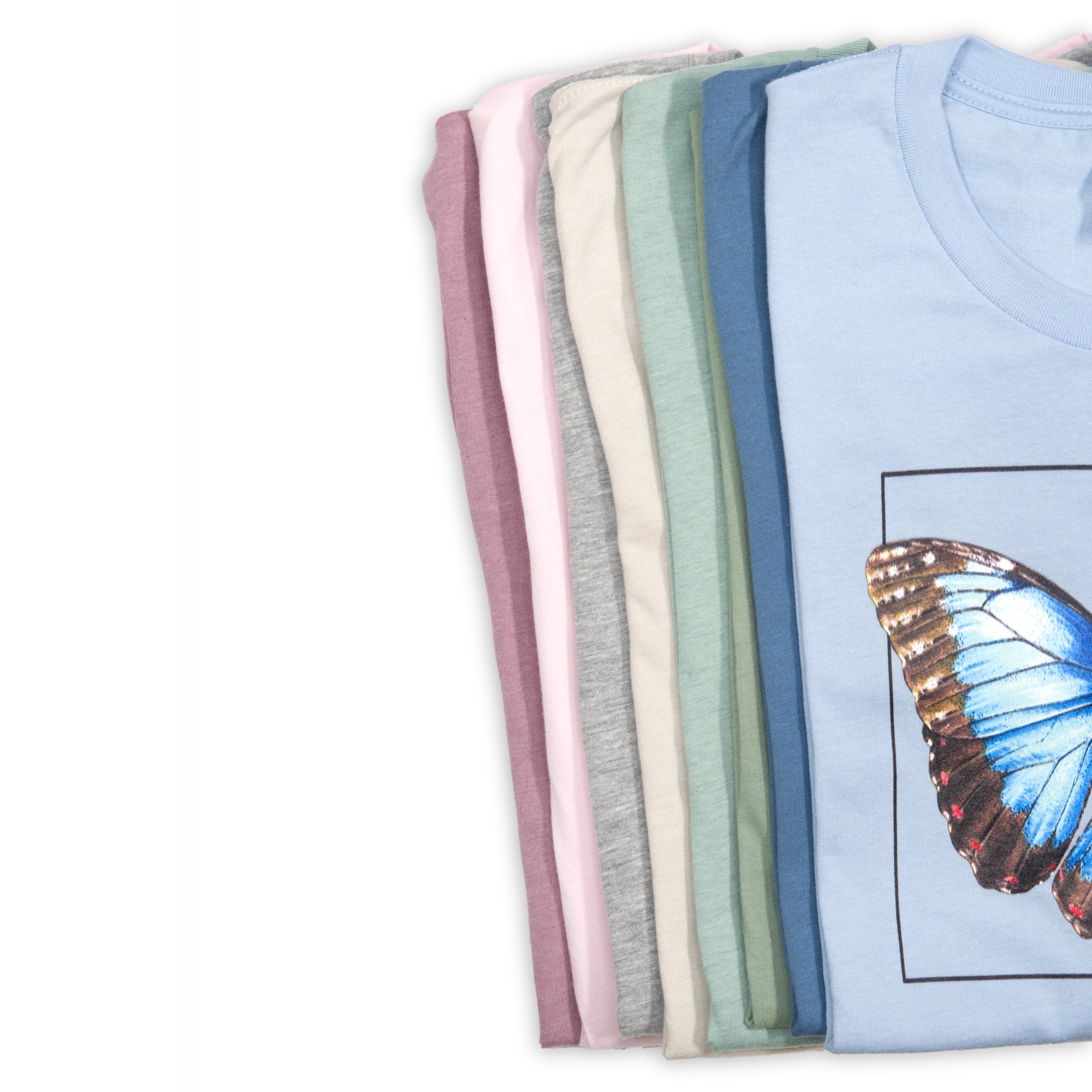 Photo of all available t-shirt colours, all shirts folded on a white surface.