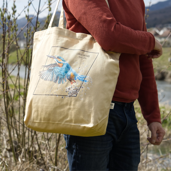 Organic tote bag featuring a common kingfisher in an outside photoshoot, hanging from the shoulders of a male model.