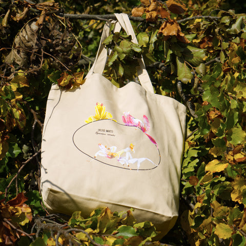 Photo of our  orchid mantis 100% organic cotton tote bag outside hanging from a branch with colourful leaves. Three colourful insects are depicted on the sturdy, spaciuos bag.