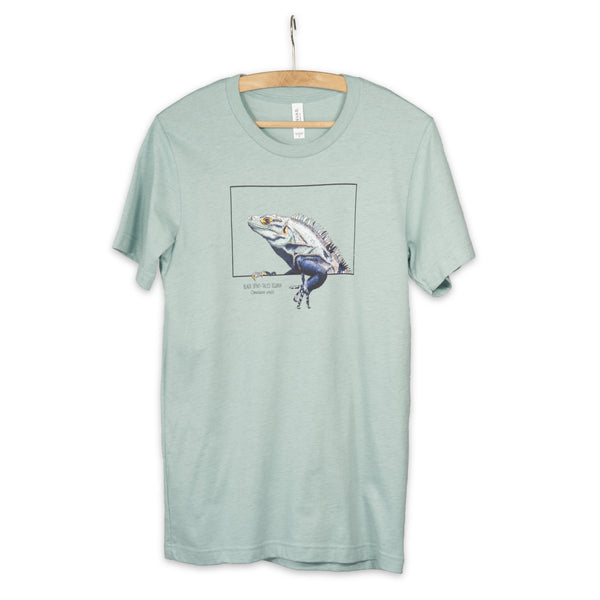 Product photo of our black iguana t-shirt on a heather prism dusty blue base colour. Hanging from a wooden hanger.