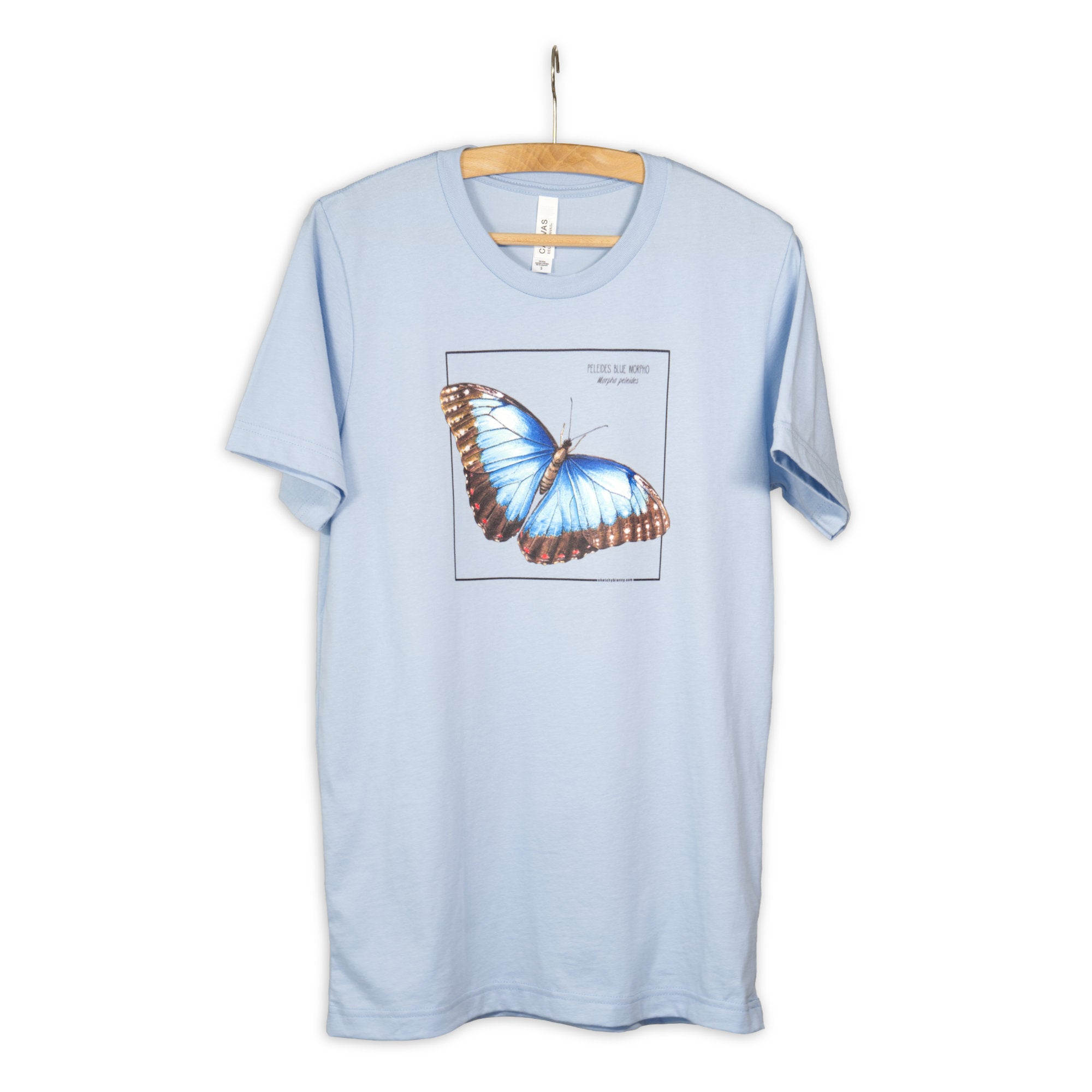 Photo of our baby blue blue morpho butterfly t-shirt hanging from a wooden hanger.