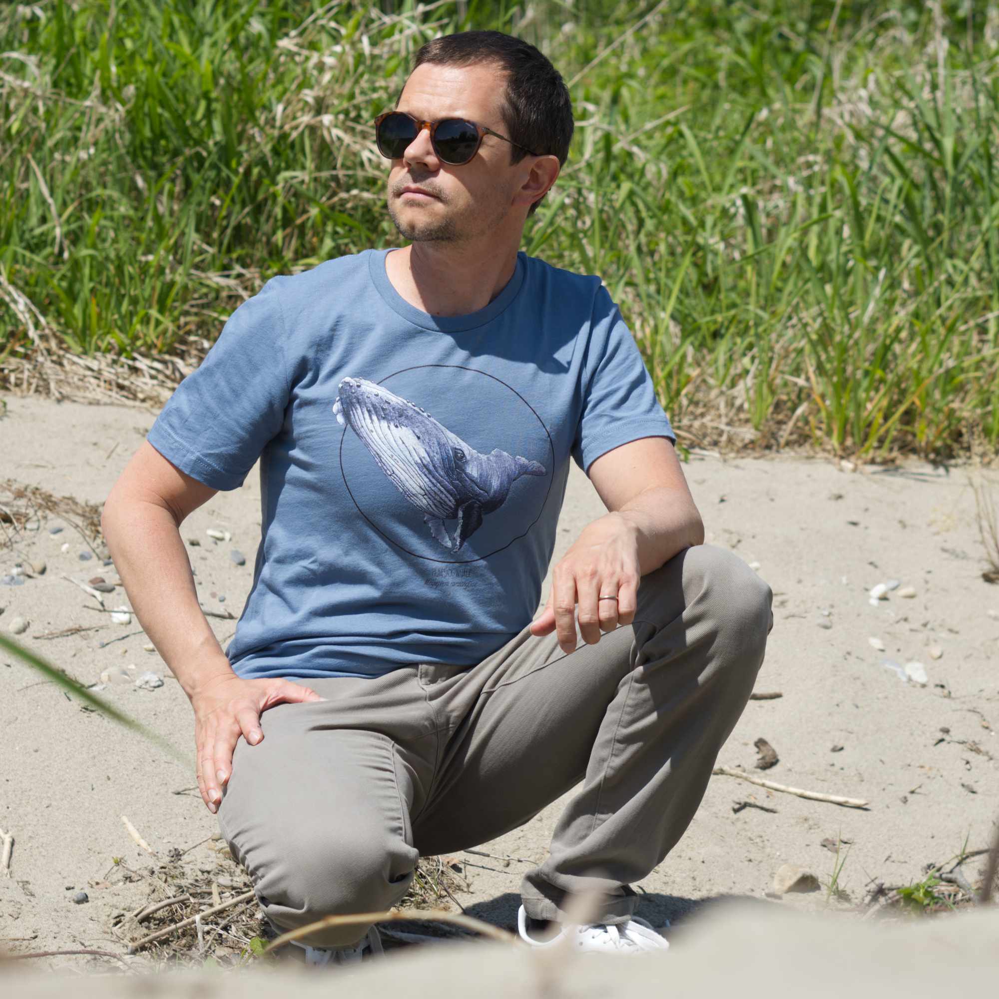 Male model outdoor on a beach wearing a steel blue t-shirt with a humpbak whale print.
