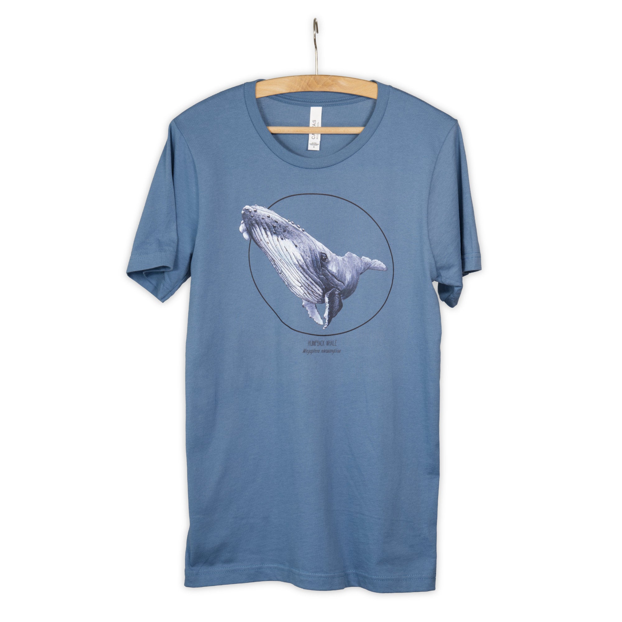 Photo of our  steel blue t-shirt with a humpbak whale print on a wooden hanger.