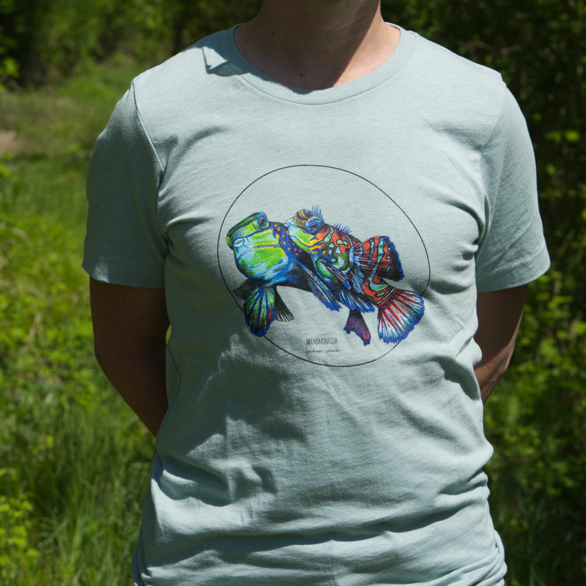 Outdoor photo of a male model wearing the heater prism dusty blue t-shirt featuring a stunning couple of mandarinfish. Shirt size is S, model is 164cm tall.