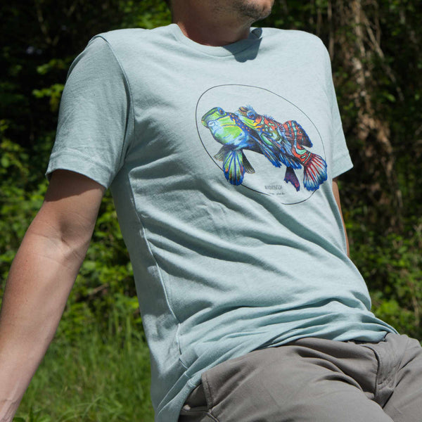 Outdoor photo of a male model wearing the heater prism dusty blue t-shirt featuring a stunning couple of mandarinfish. Shirt size is S, model is 164cm tall.