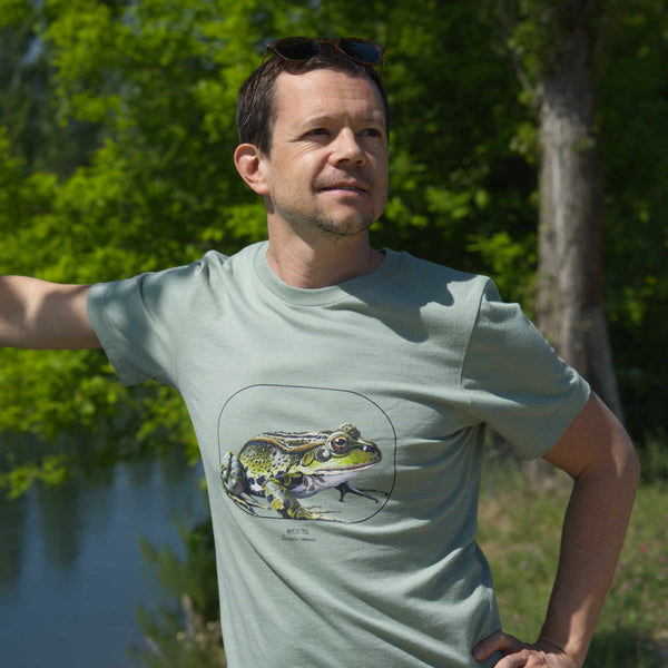 Photo of a male model leaning against a tree, wearing a sage coloured t-shirt with a beautiful marsh frog print.