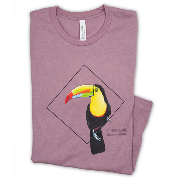Photo of our stunning keel-billed toucan print, here on a heather orchid coloured t-shirt folded on a white surface.